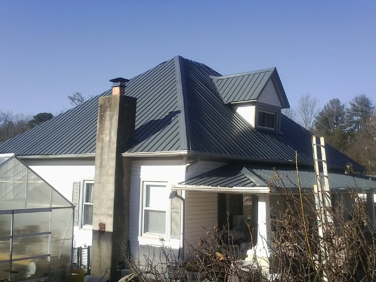 Dark blue standing seam metal roof on a white farmhouse with dormer — Slate & Tile Roof Repair by Roofing Brothers in Nacogdoches