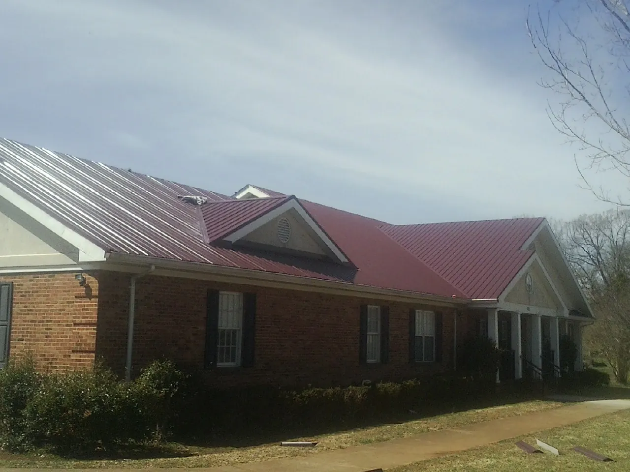 Red metal roof with gabled entries on a long brick building, from a Hail Damage Roof Repair job in Nacogdoches