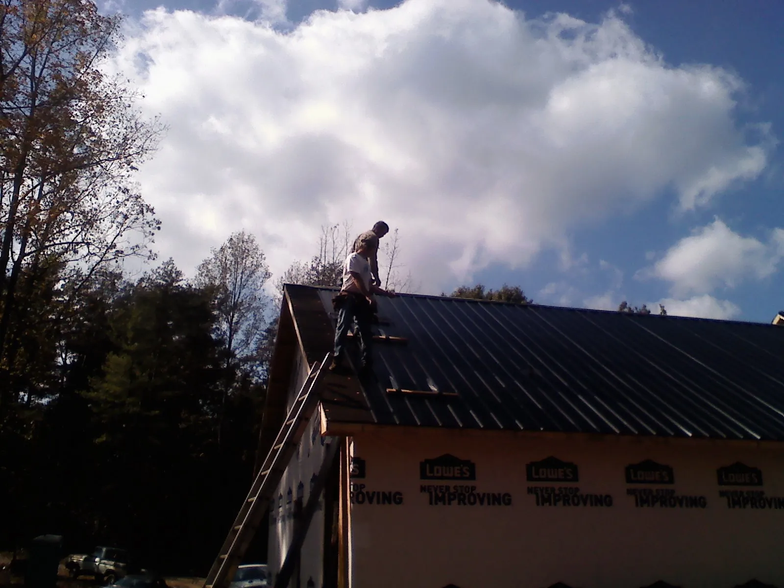 Roofer fastening dark metal panels high against a cloudy sky, from a Roof Inspection job in Nacogdoches