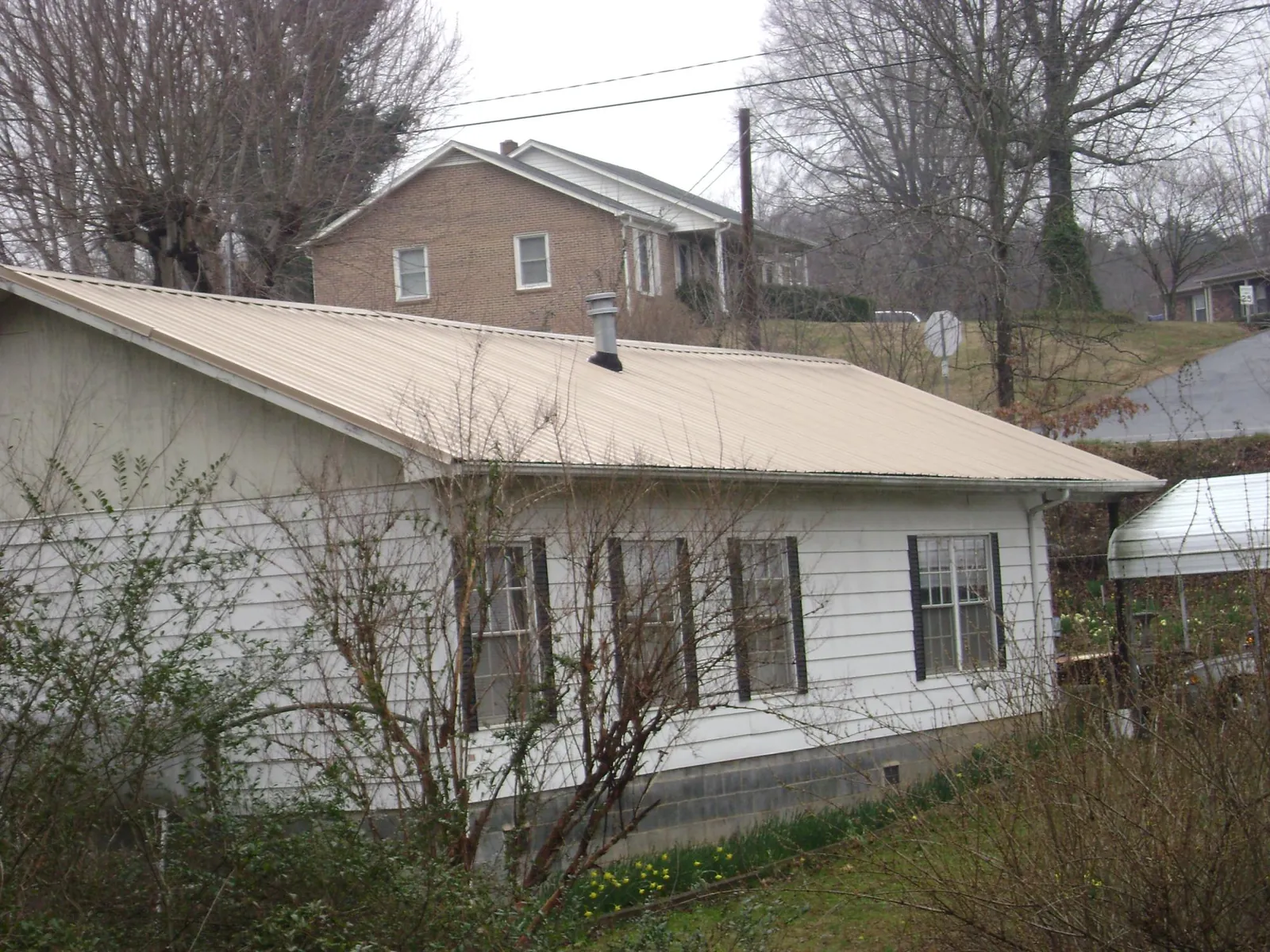 Tan metal roof on a white sided house set into a hillside — Commercial Roofing by Roofing Brothers in Nacogdoches