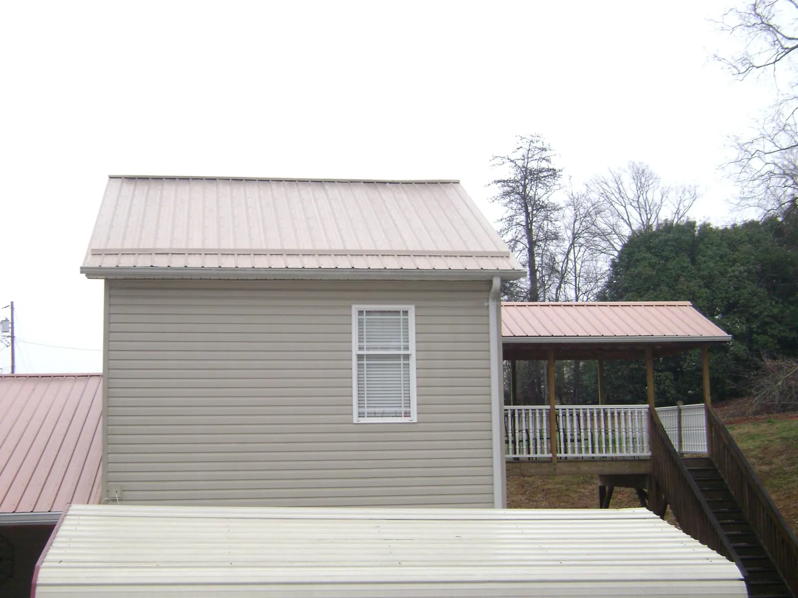 Tan metal roofs on a two story addition and attached porch, from a Roof Replacement job in Nacogdoches